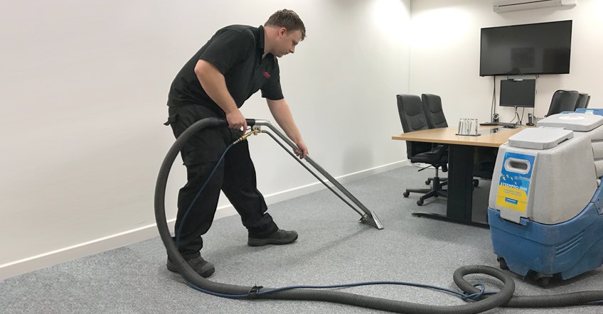 Technician deep-cleaning commercial office carpet with a hot-water extractor